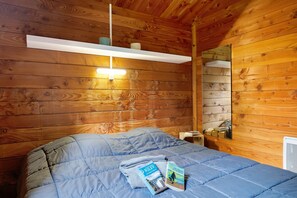 Une chambre dans une cabane en bois, avec un lit, une étagère avec une lampe et un miroir.