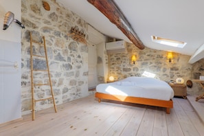 A bedroom with a stone wall, wooden bed frame, ladder, and a skylight. - Guest Room "Le Pigeonnier" with Shared Pool, Wi-Fi, and Air Conditioning (Saint-Alban-Auriolles)