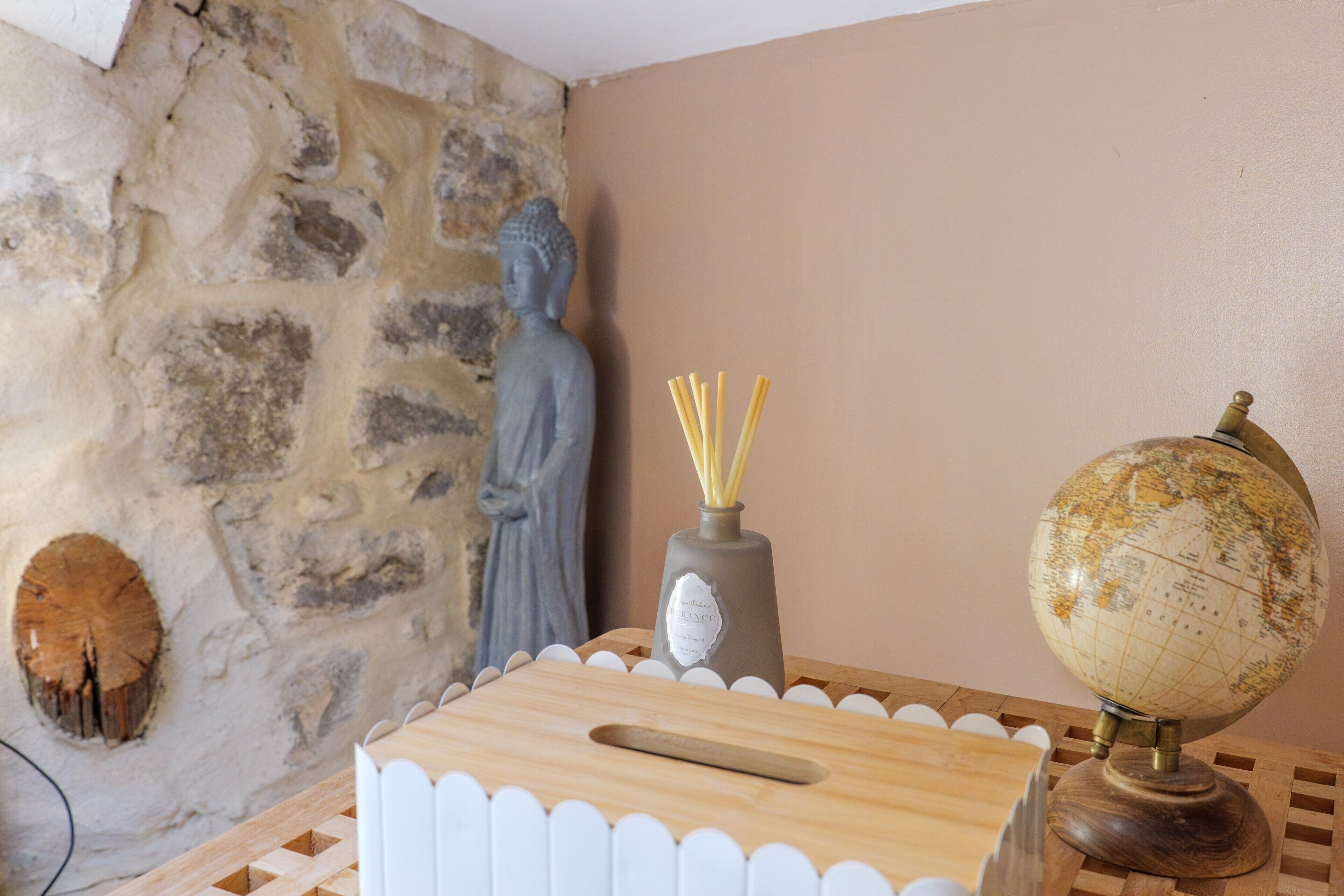 Ein Zimmer mit Steinwand, Buddha-Statue, Globus und einer Vase mit Schilfrohren.