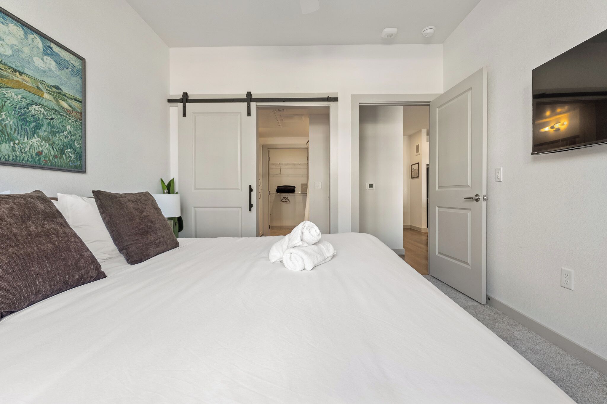 Camera d'albergo con un letto grande, biancheria bianca, un quadro appeso e una porta scorrevole che dà su un bagno.