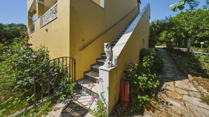 A yellow building with a staircase leading to a balcony, surrounded by greenery and a stone pathway. - Studio Apartment 'With Seaview 1' with Sea View, Wi-Fi and Air Conditioning (Limni)