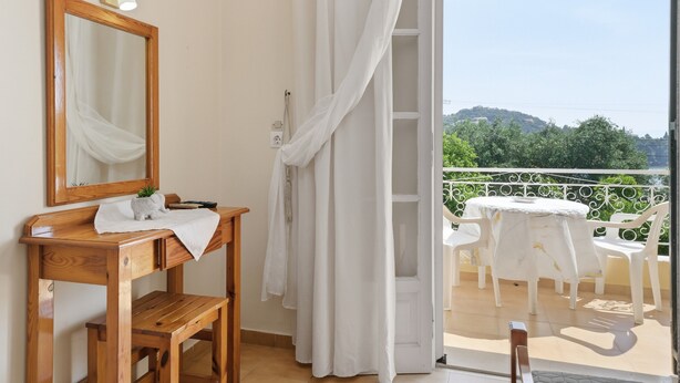 A room with a wooden desk, a mirror, a small plant, and a balcony with a table and chairs. - Studio 'Garden View 4' with Sea View, Wi-Fi and Air Conditioning (Limni)