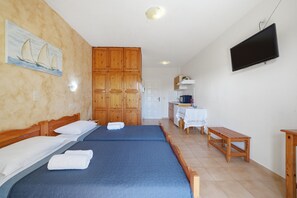 A hotel room with two beds, wooden cabinets, a television, and a small table. - Studio 'Garden View 4' with Sea View, Wi-Fi and Air Conditioning (Limni)