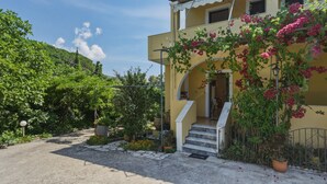 A yellow building with a white staircase, surrounded by greenery and potted plants. - Studio 'Garden View 4' with Sea View, Wi-Fi and Air Conditioning (Limni)