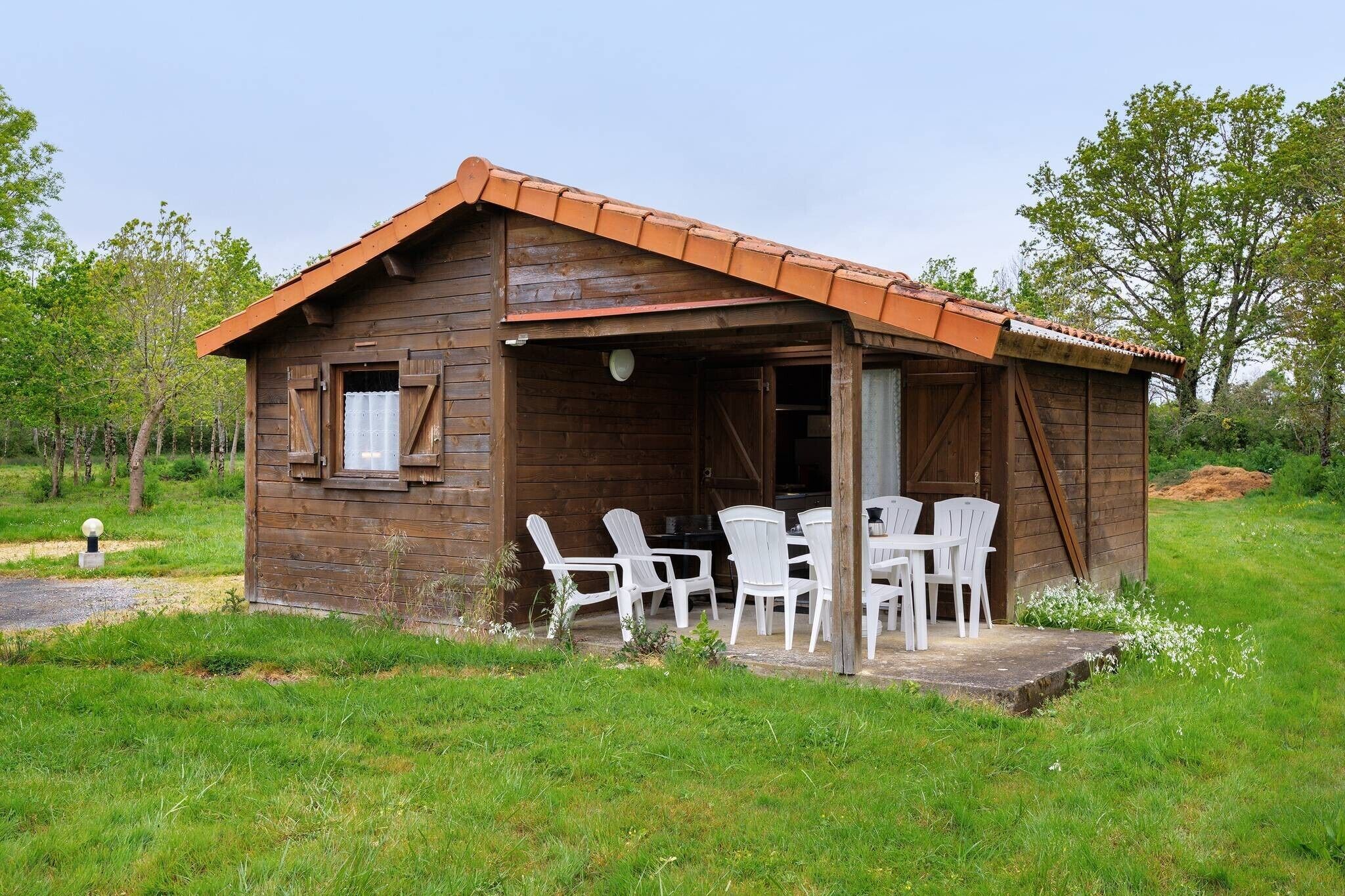 A wooden cabin with a porch, white plastic chairs, and a small table.