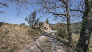 A rural stone building with a dirt path leading to it, surrounded by trees and hills. - Casa Rural La Moixella: Catalan Country House with Private Pool and Pyrenees Views (Lladurs)