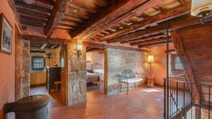A rustic room with exposed wooden beams, a stone wall, a bed, a bench, and a trash can. - Casa Rural La Moixella: Catalan Country House with Private Pool and Pyrenees Views (Lladurs)