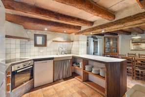 A kitchen with exposed wooden beams, a built-in oven, a dishwasher, and a tiled backsplash. - Casa Rural La Moixella: Catalan Country House with Private Pool and Pyrenees Views (Lladurs)