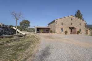 A stone building with a gravel driveway, a wooden bench, and two potted plants. - Casa Rural La Moixella: Catalan Country House with Private Pool and Pyrenees Views (Lladurs)