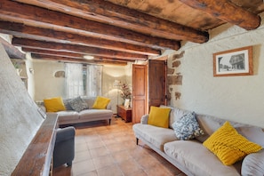 A cozy living room with a sofa, a wooden bench, and a wooden ceiling. - Casa Rural La Moixella: Catalan Country House with Private Pool and Pyrenees Views (Lladurs)