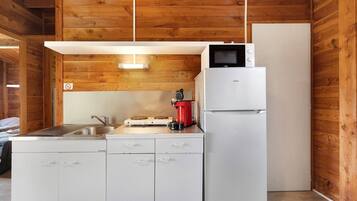 Een compacte keuken met houten wanden, een witte koelkast, een magnetron, een koffiezetapparaat en een spoelbak.
