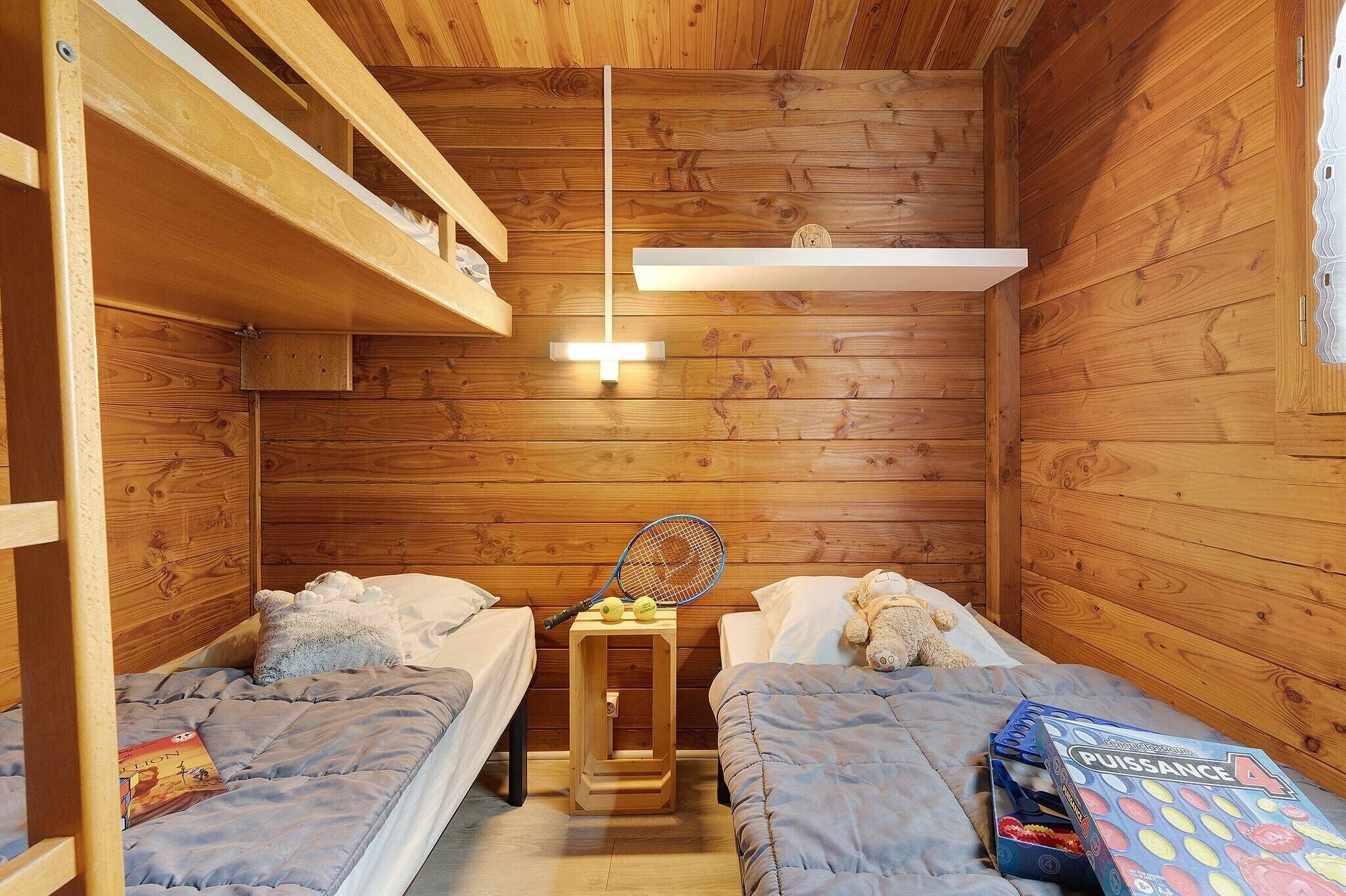 A wooden cabin room with bunk beds, a small table with a tennis racket and balls, and a board game.
