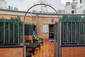 Une terrasse extérieure avec une table et des chaises, un mur en briques et un portail en métal.