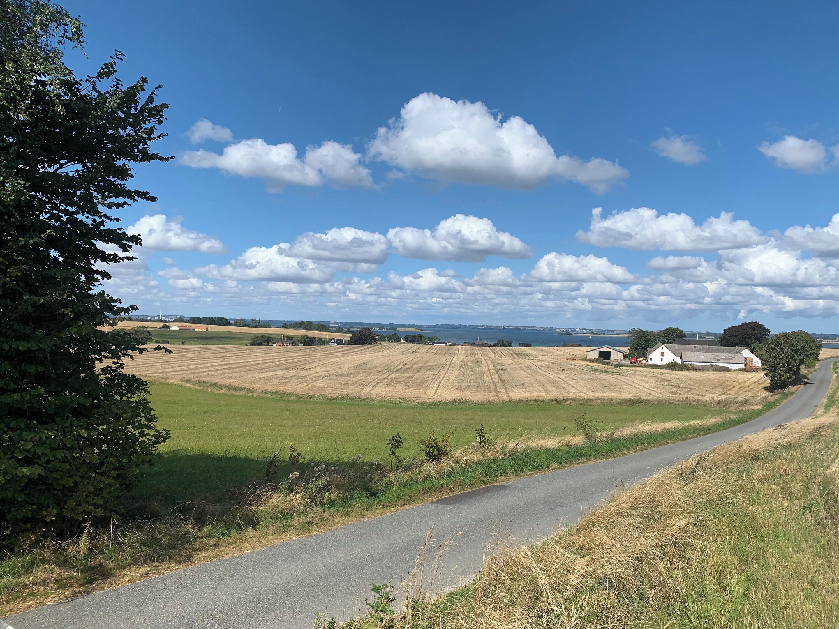 Un paysage rural avec une route, des champs et quelques bâtiments dispersés.