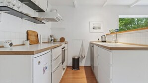 Een kleine keuken met witte apparaten, houten aanrecht en een raam met uitzicht op bomen.
