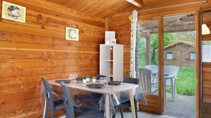 Eine Holzhütte mit einem Esstisch für vier Personen, einem weißen Schrank und einer Schiebetür zu einem Außenbereich.