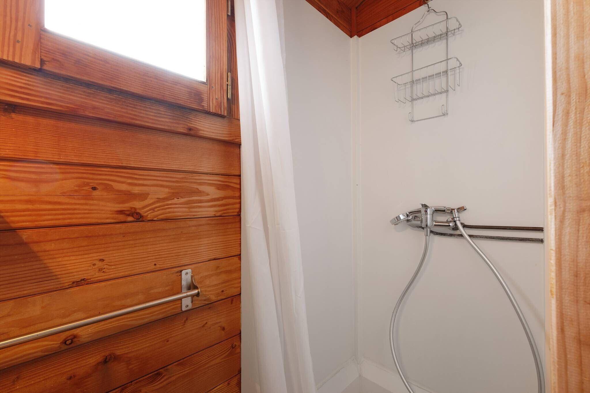 Ein Badezimmer mit Holzwänden, einer Dusche, einem Handtuchhalter und einem Fenster.