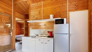 A compact kitchen with a microwave, stove, and refrigerator, wooden walls, and a sliding door leading to another room. - Chalet "Confort 12" with Terrace and Shared Pool (Saint-Gervais)