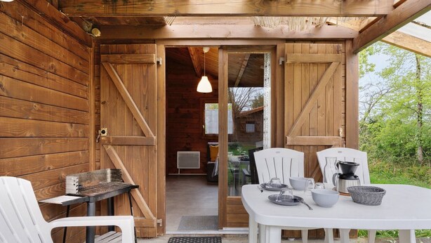 A wooden cabin with a dining area featuring a table, chairs, and a grill. - Chalet "Confort 12" with Terrace and Shared Pool (Saint-Gervais)