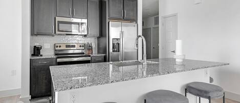A modern kitchen with dark cabinets, stainless steel appliances, a granite countertop, and bar stools.