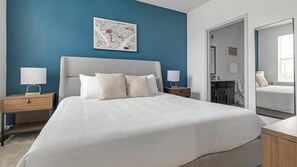 A modern bedroom with a large bed, two bedside tables with lamps, a blue accent wall, and a framed artwork above the bed. - Landing | Stunning 2BD, Pool, Gym (Austin)