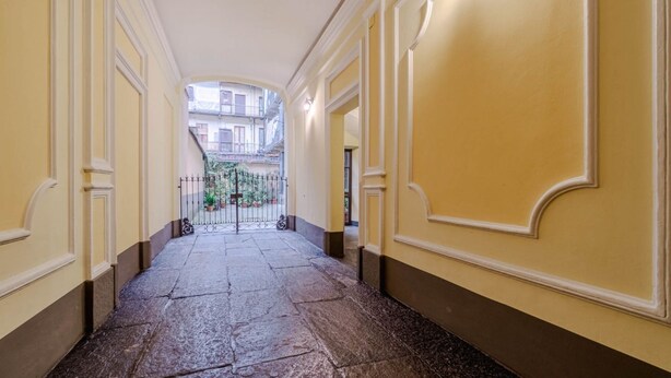 A corridor with a stone floor, yellow walls, and a view of a building with balconies.