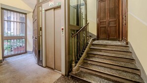 A hotel lobby with a staircase, an elevator, and a large wooden door.
