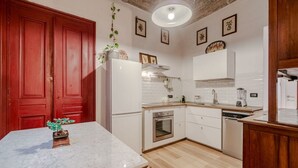 A kitchen with white cabinets, a marble countertop, a red door, and a hanging plant.