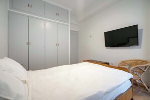 Ein Schlafzimmer mit einem Bett, einem Kleiderschrank, einem Fernseher und einem Korbstuhl.