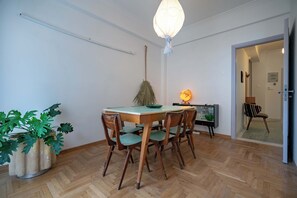 A dining area with a wooden table and chairs, a hanging light fixture, and a potted plant. - Artistic Bright Apartment – Attiki Metro by ΜΡS (Athina)