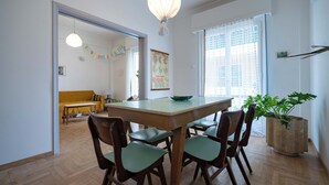 A dining area with a wooden table and chairs, a hanging light fixture, and a potted plant. - Artistic Bright Apartment – Attiki Metro by ΜΡS (Athina)