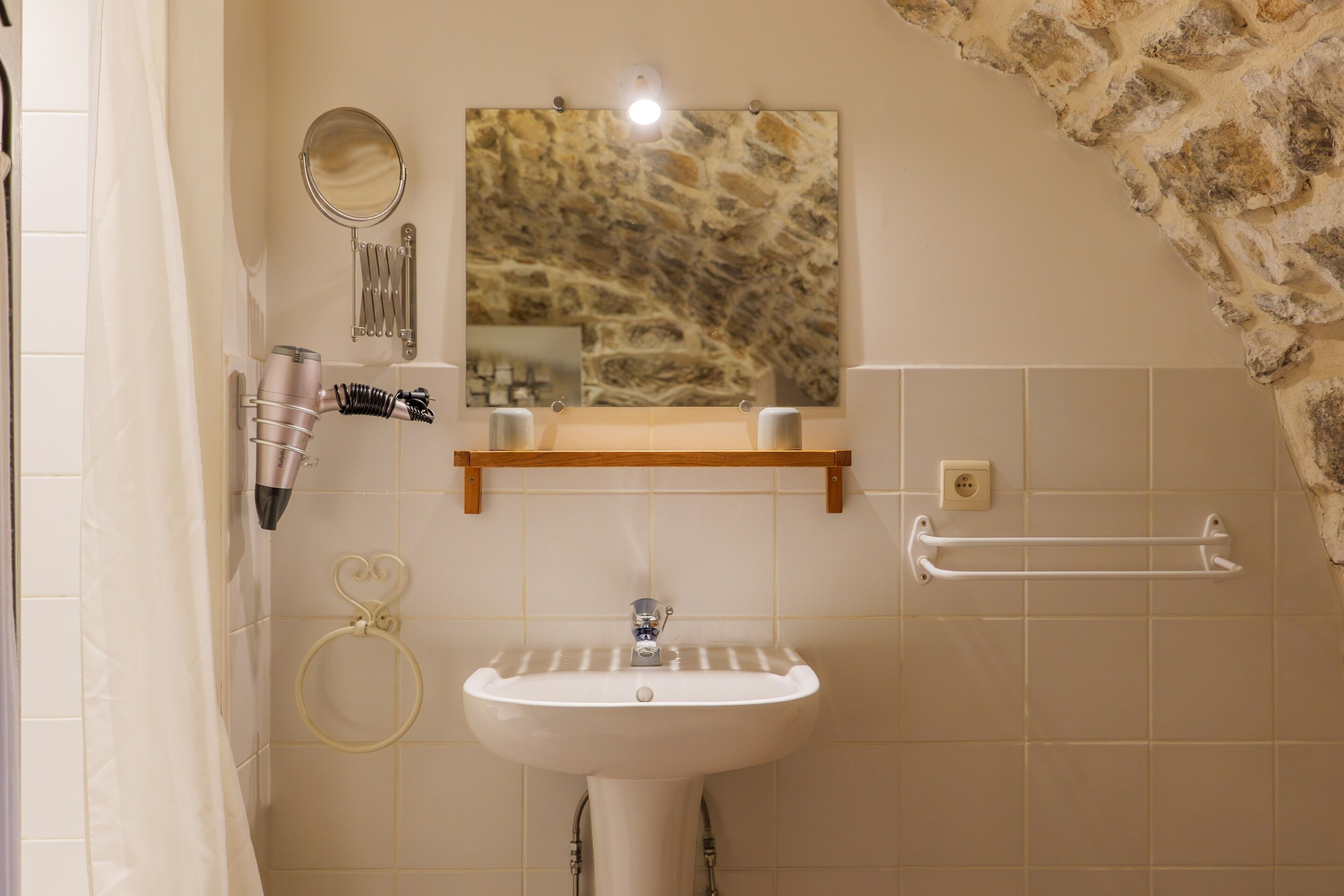 Une salle de bain avec un lavabo blanc, un miroir, un porte-serviettes et un mur en pierre.