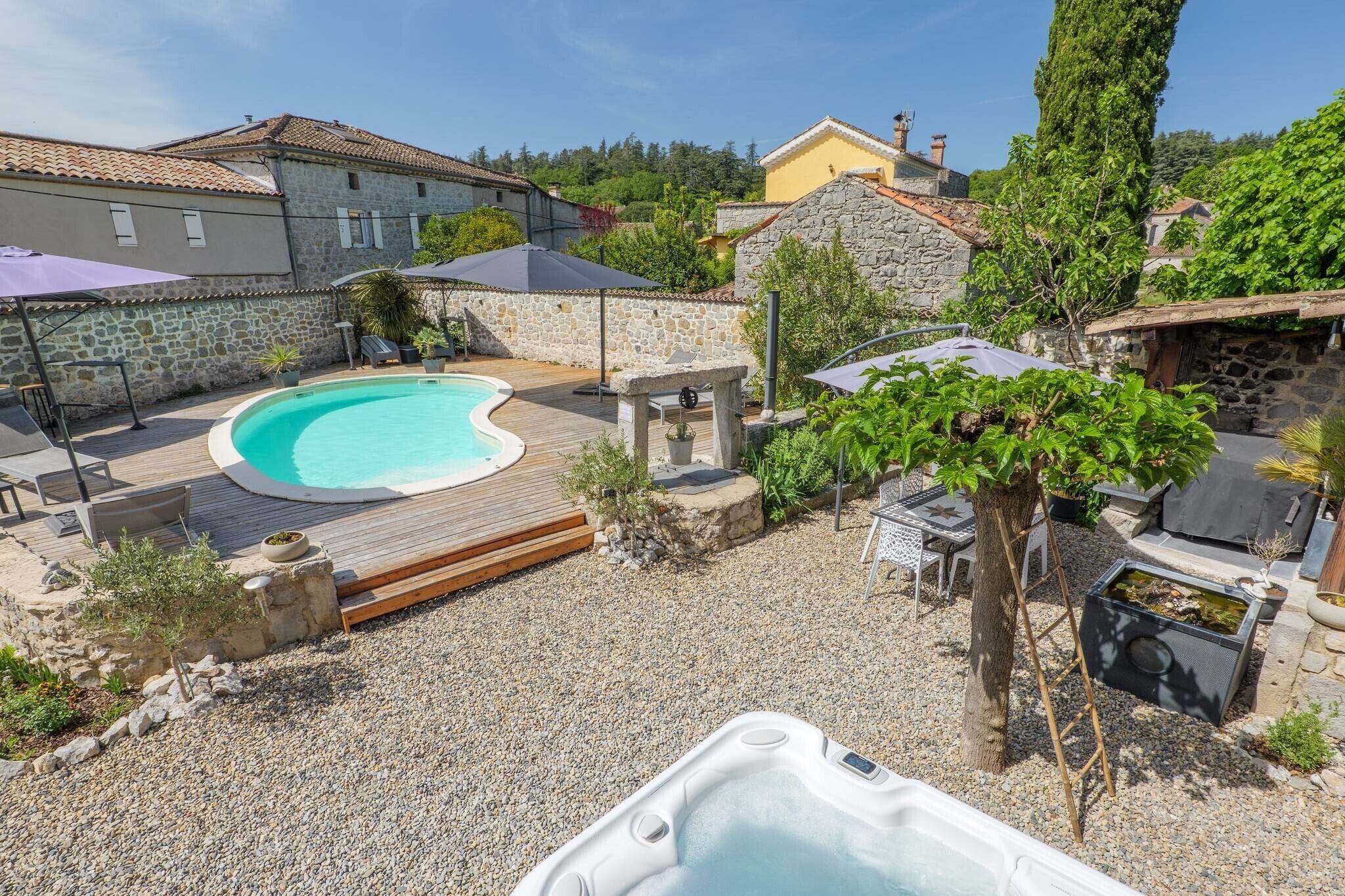 A backyard with a swimming pool, hot tub, and stone walls.
