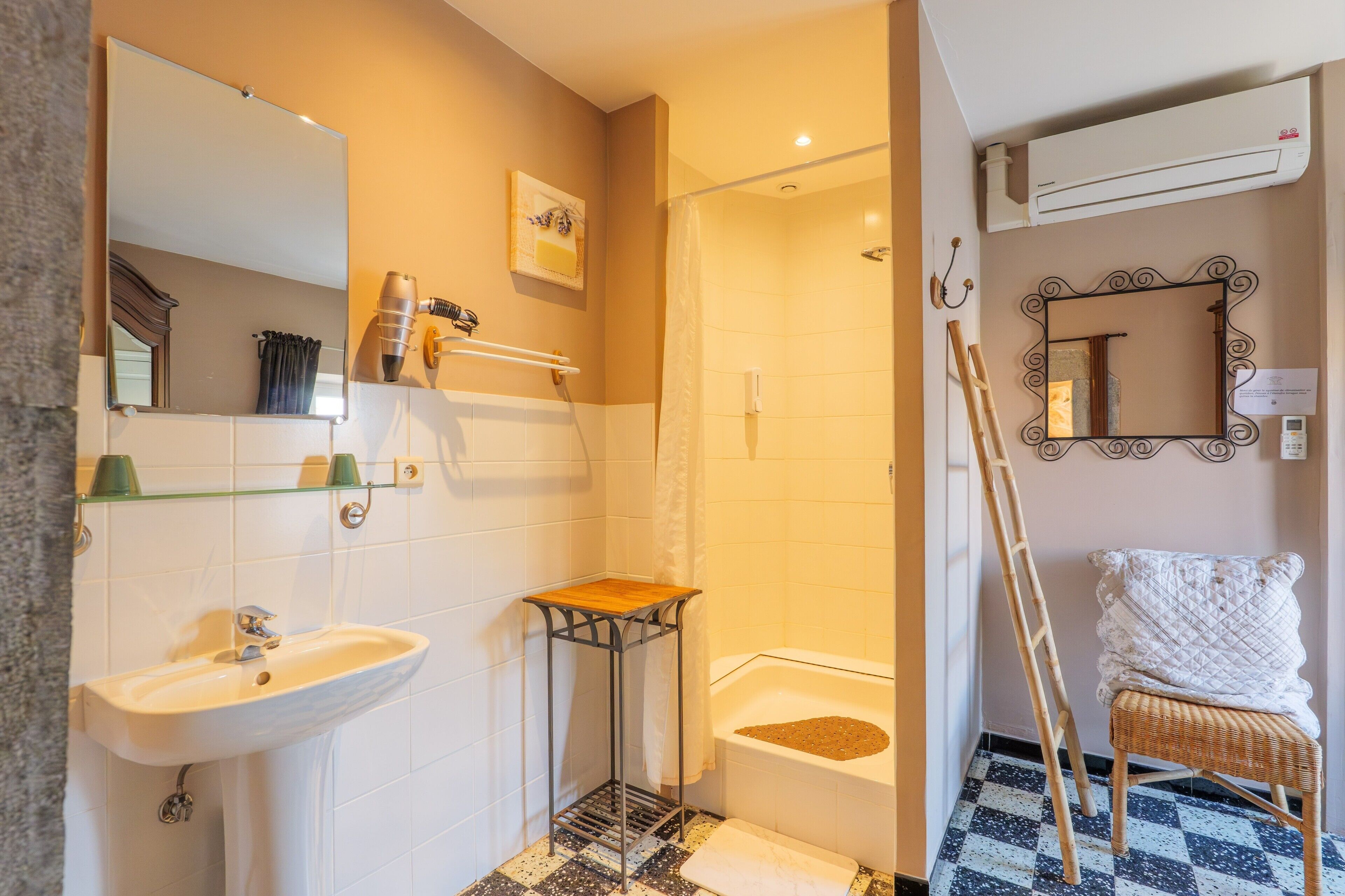 A bathroom with a sink, mirror, shower, and a small wooden stool.