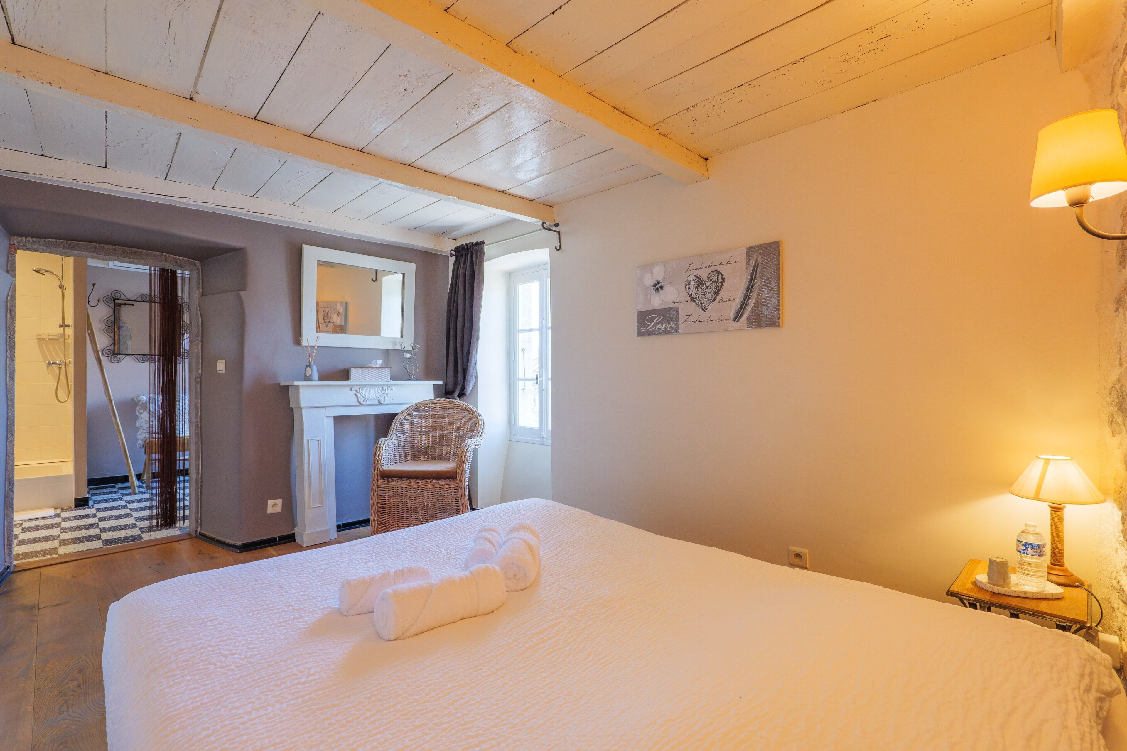 A hotel room with a bed, a desk, a chair, a bathroom, and a wall-mounted lamp.