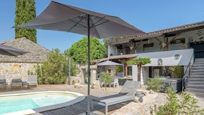 Zona de piscina con sillones de descanso, una pérgola y un edificio de piedra con techo de tejas.