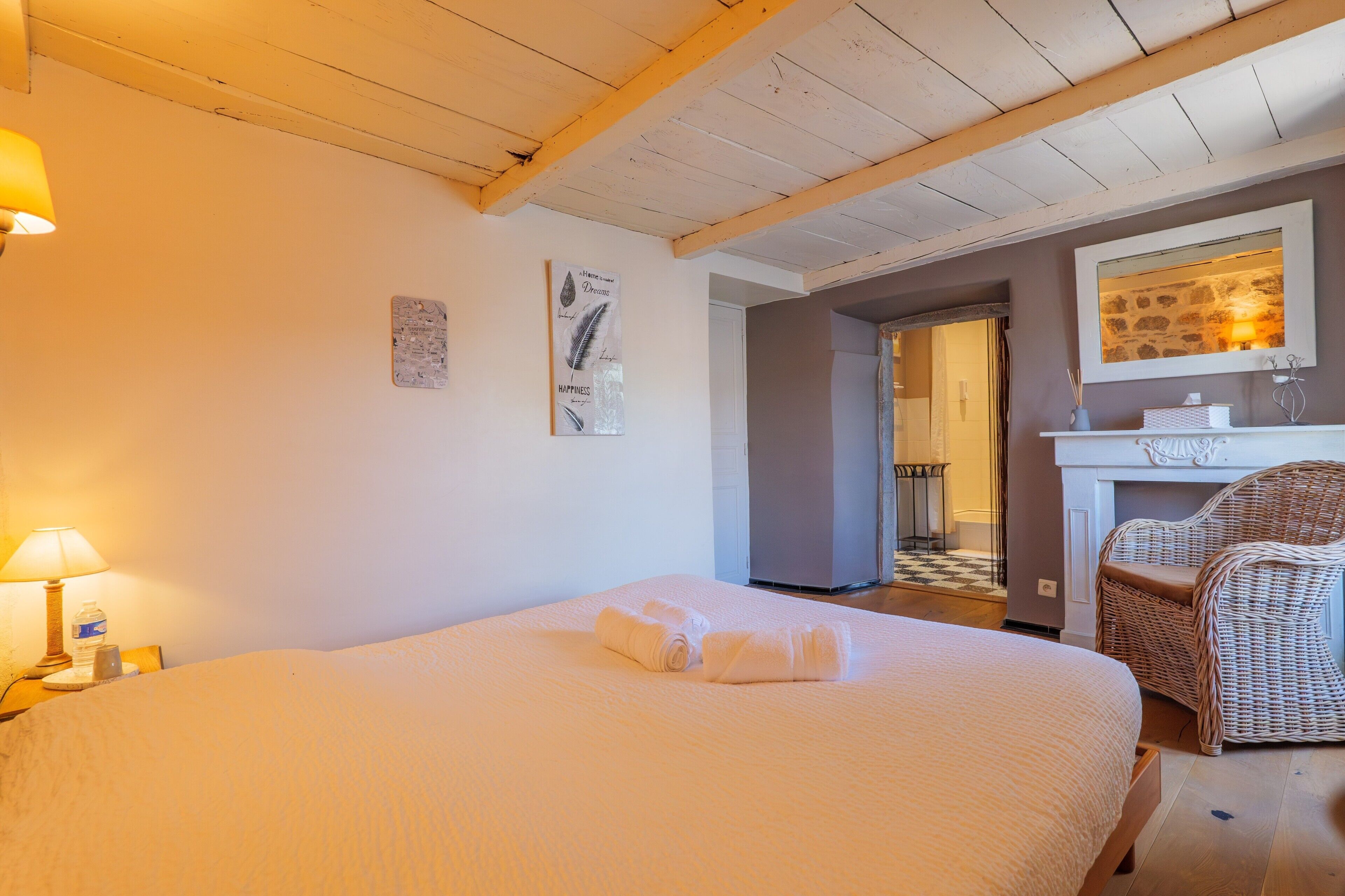 A bedroom with a bed, a lamp, a chair, and a fireplace.