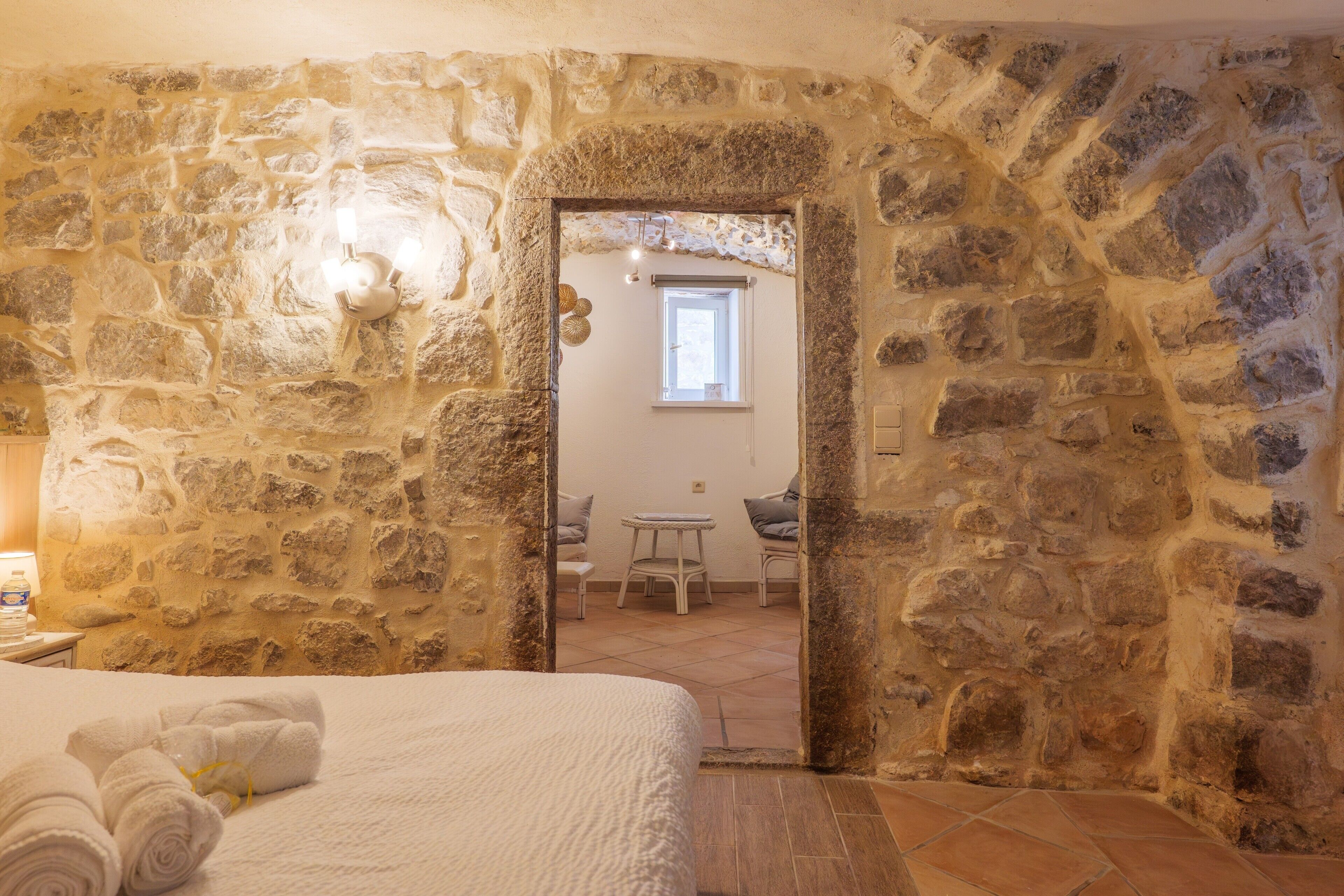 Una stanza con pareti in pietra, un letto, un tavolino e una sedia.