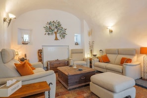 A living room with a sofa, armchairs, a wooden coffee table, and a decorative tree wall art.