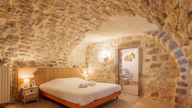 A bedroom with a stone wall, wooden bed frame, bedside lamps, and a nightstand.
