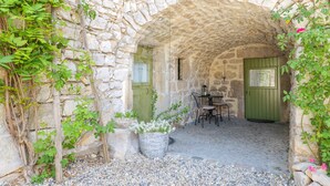 An arched stone structure with a table and chairs, a door, and potted plants.