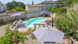 A swimming pool with a wooden deck, stone walls, and outdoor furniture.