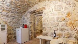 A stone-walled room with a white refrigerator, a bench, and a table with a wine bottle.