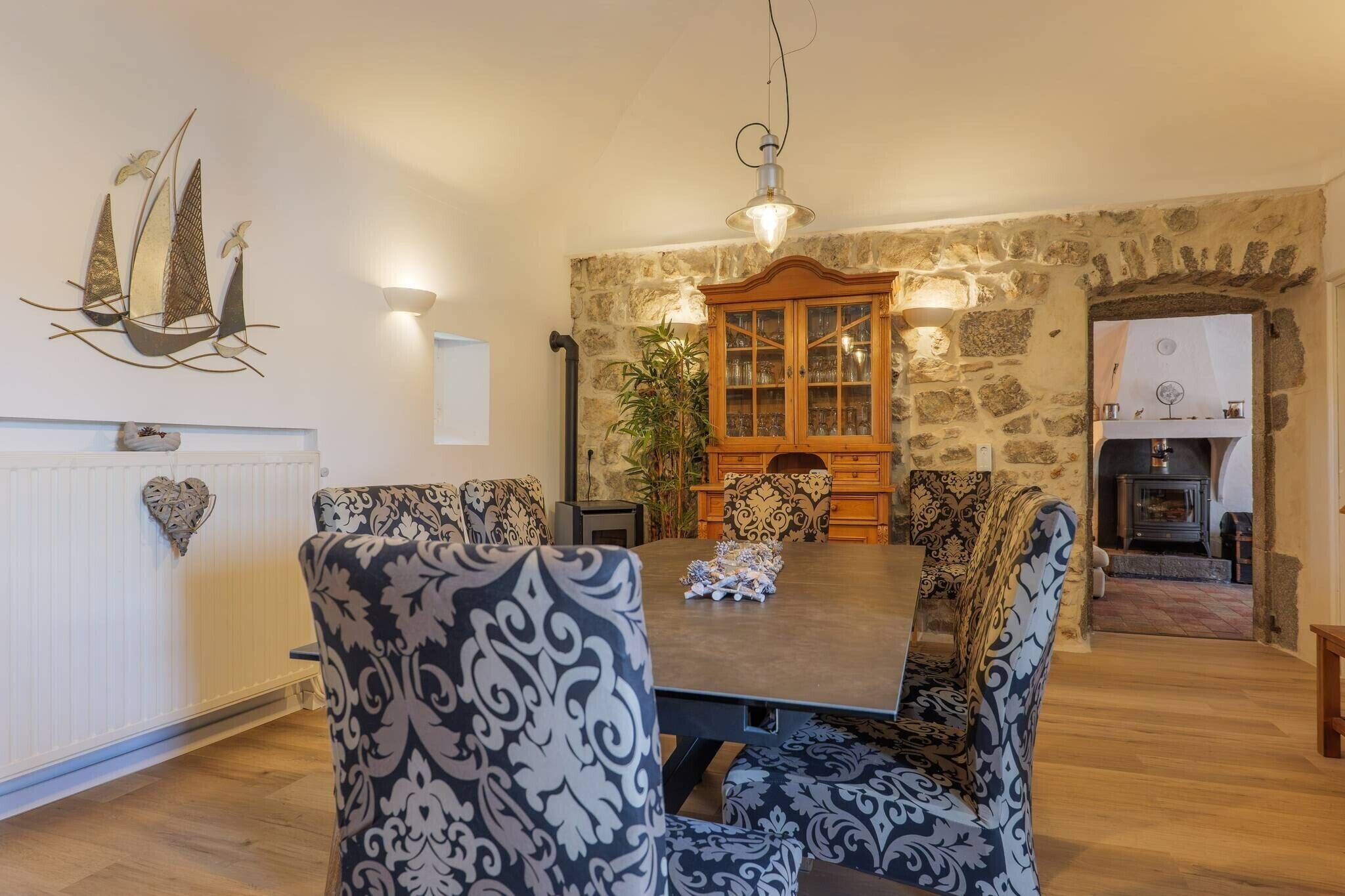 A dining room with a wooden table, patterned chairs, a decorative wall piece, and a stone wall.