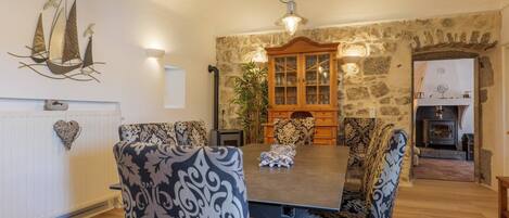 A dining room with a wooden table, patterned chairs, a decorative wall piece, and a stone wall.