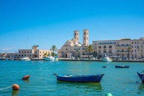 Un pueblo costero con una iglesia destacada que cuenta con dos torres, un puerto deportivo con varias embarcaciones y un cielo azul despejado.