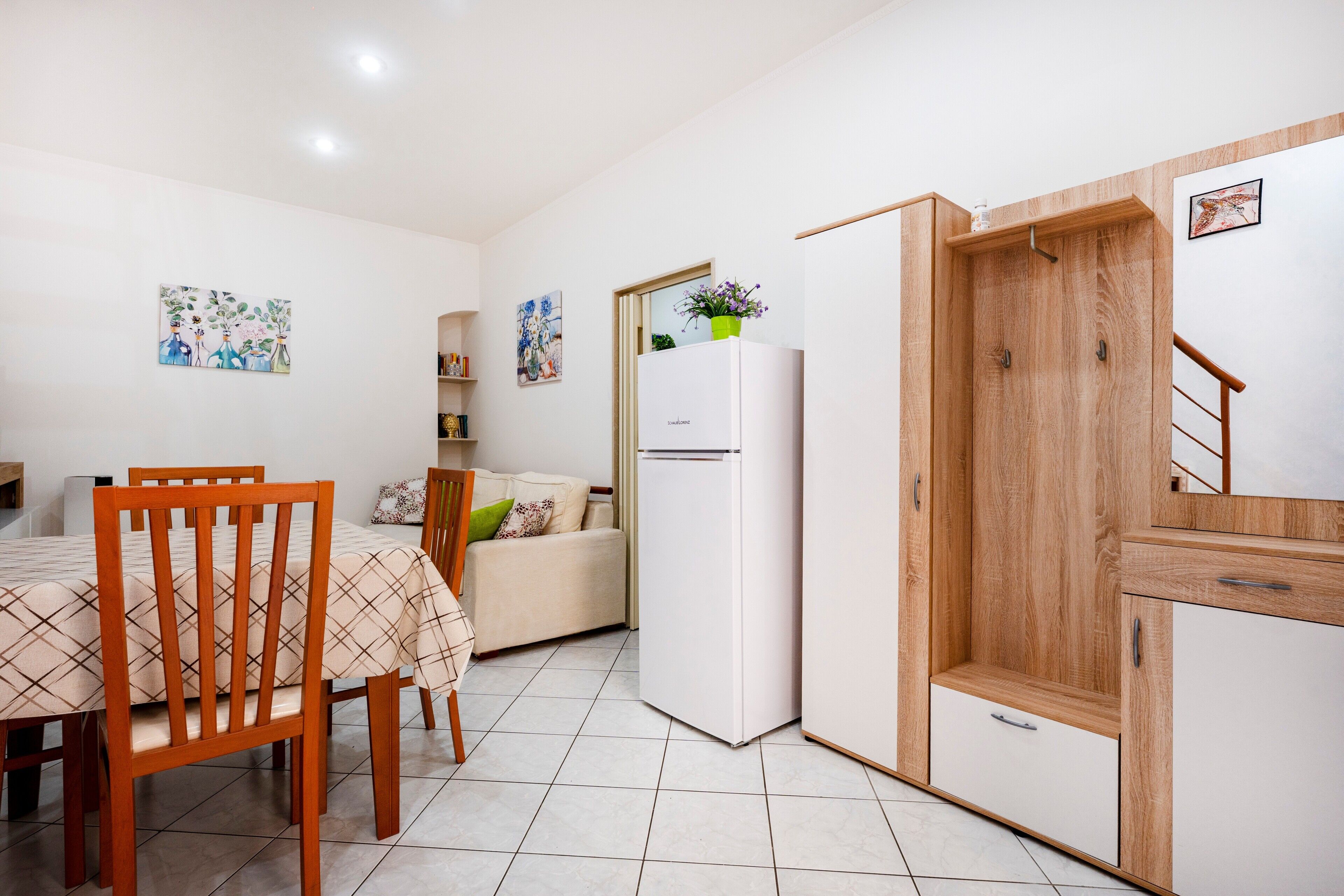 A compact living space with a dining area, a sofa, a refrigerator, and a wooden cabinet.