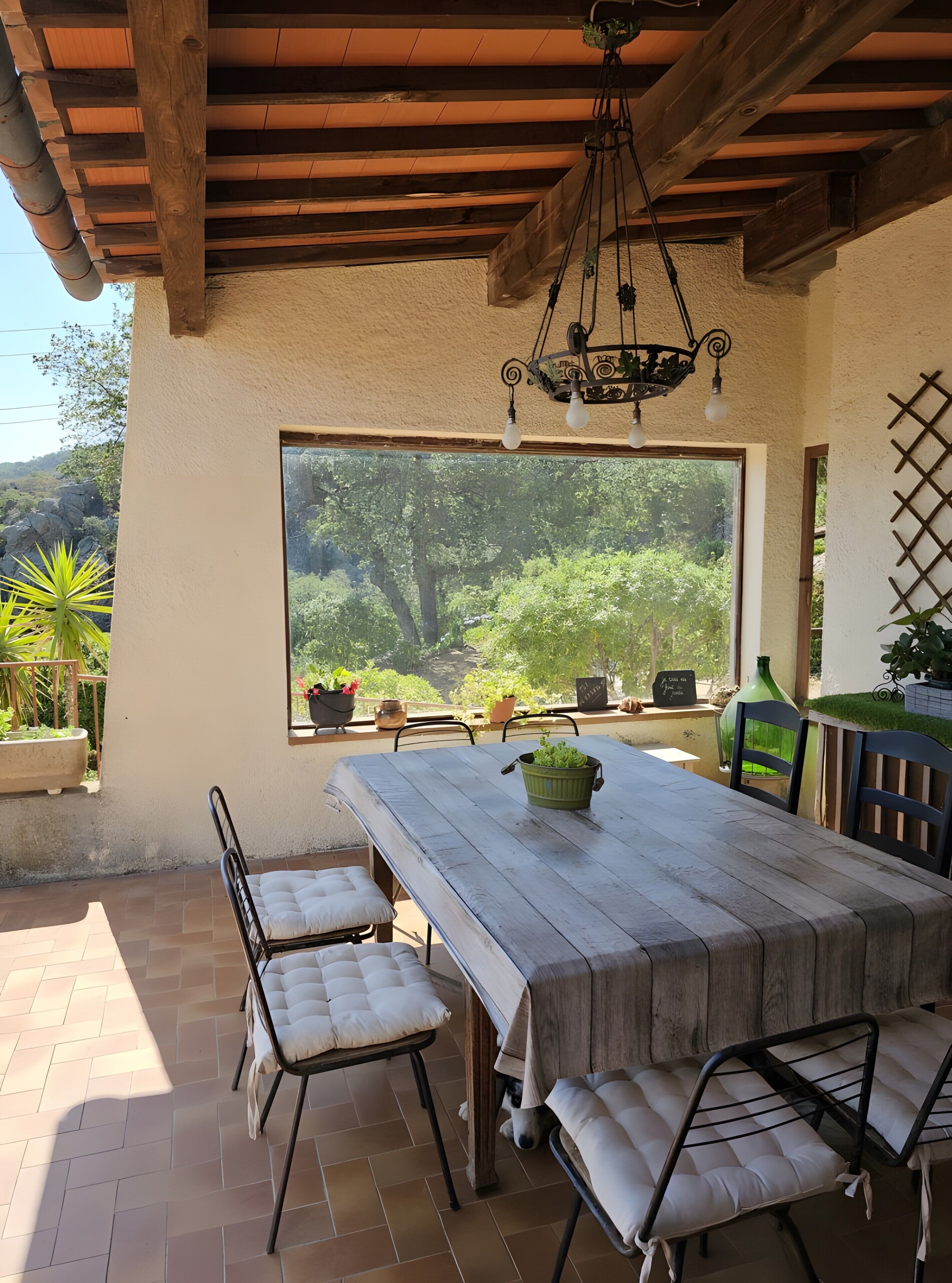A patio with a wooden table, chairs, and a view of greenery.