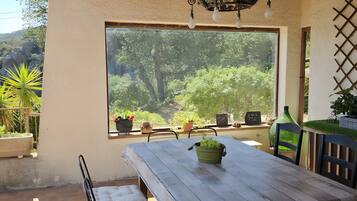 A patio with a wooden table, chairs, and a view of greenery.