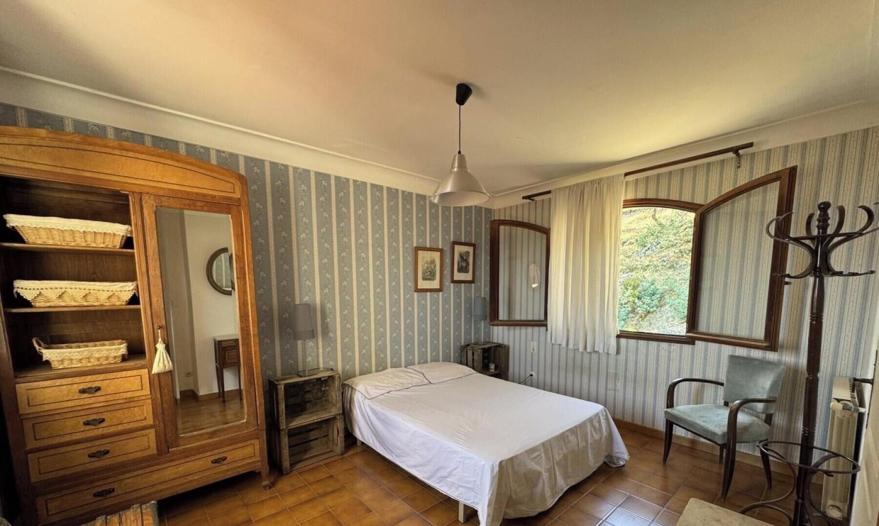 A bedroom with a bed, a wooden wardrobe, a chair, a window, and a radiator.